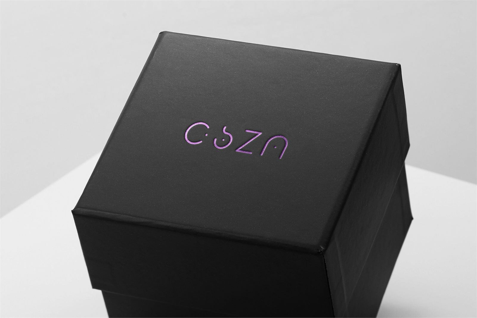 CSZN monoline logo embossed in purple foil on a matte black gift box